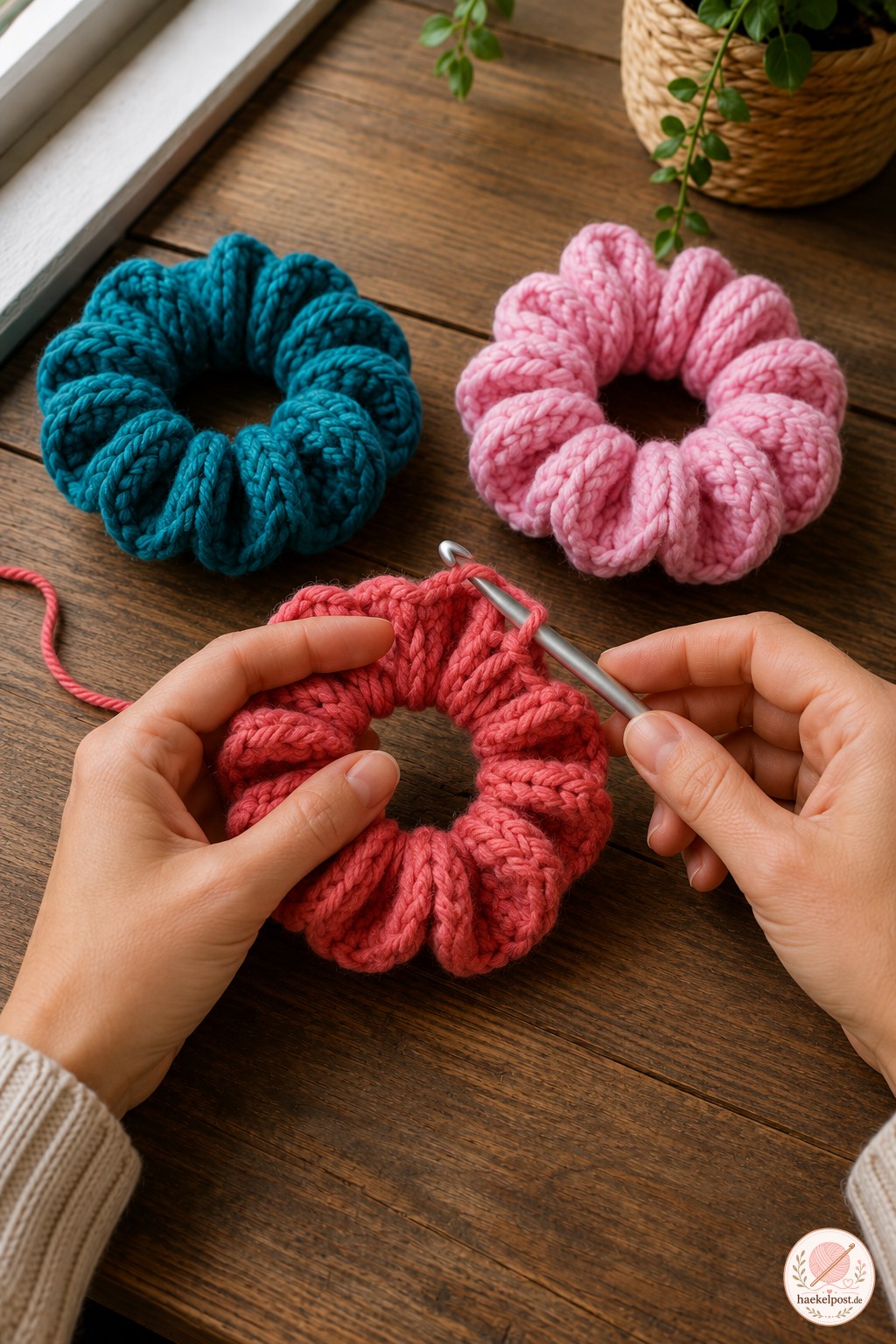 Koralle Scrunchie wird fertiggehäkelt, daneben liegen bereits zwei fertige gekräuselte Scrunchies