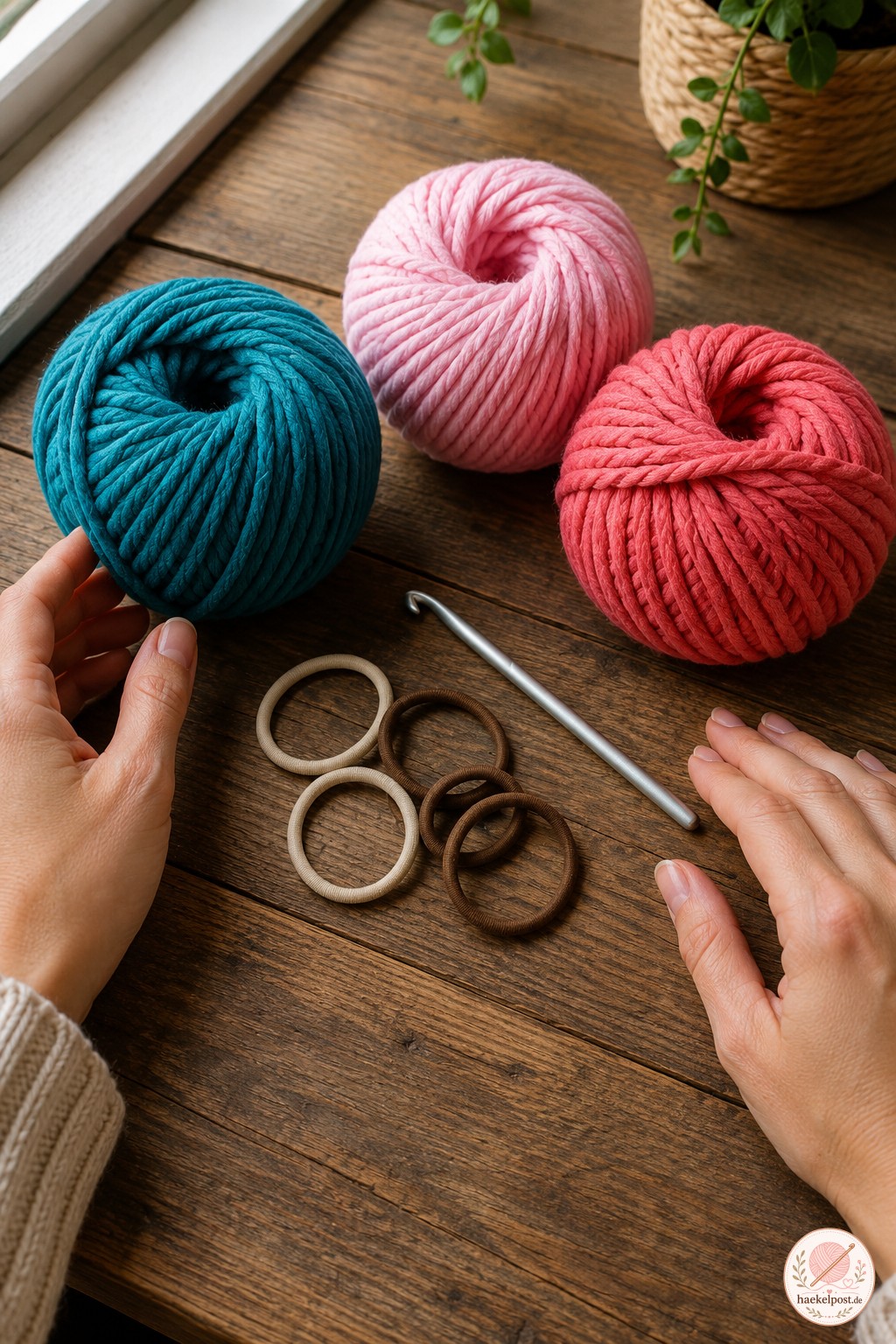 Wollknäuel in Teal, Rosa und Koralle sowie Gummibänder liegen bereit, um eine gekräuselte Scrunchie zu häkeln