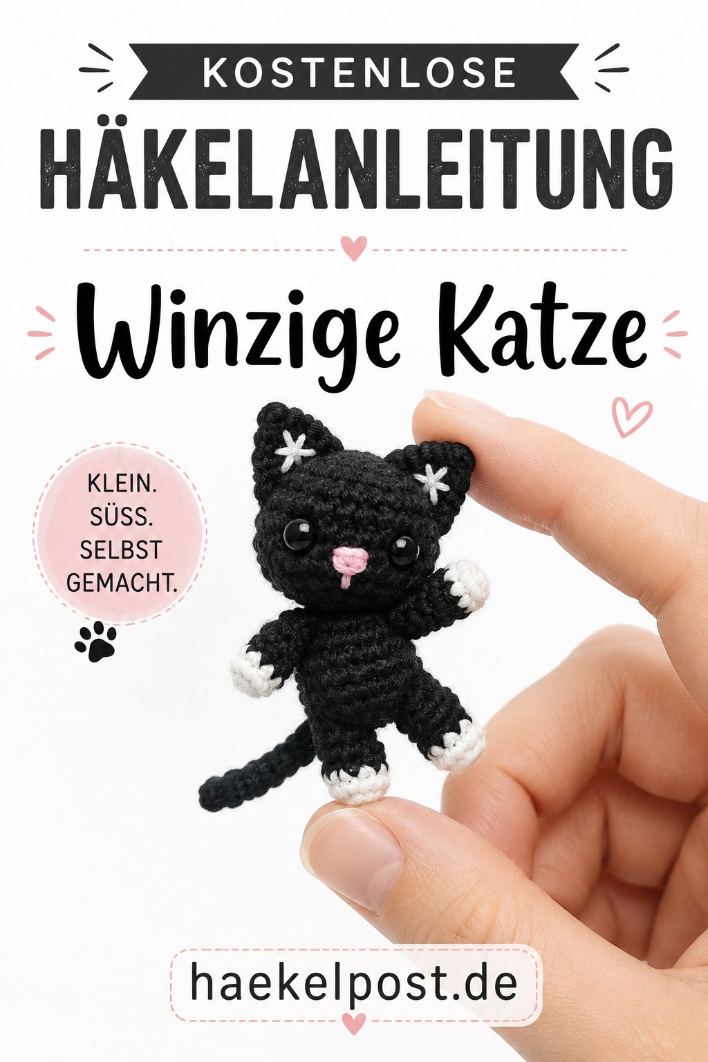 Eine winzige schwarze gehäkelte Mini-Katze mit weißen Pfoten steht klein und selbstgemacht auf einer Fingerspitze.