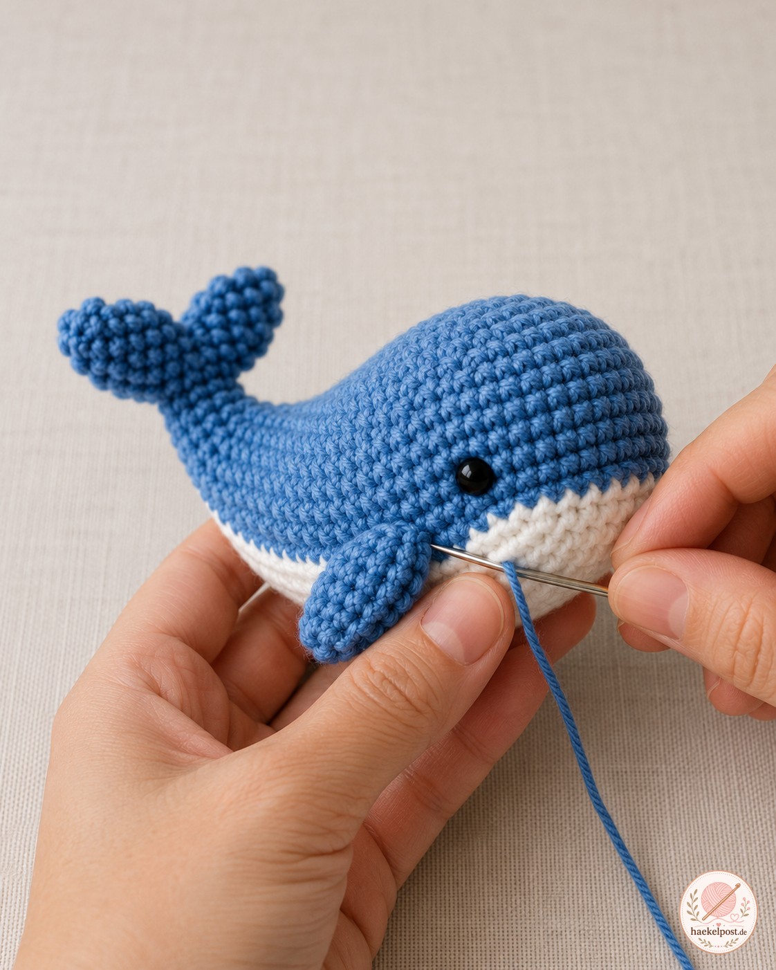 Weißer Bauch und kleine Flossen werden mit der Nadel an den Amigurumi-Wal genäht.